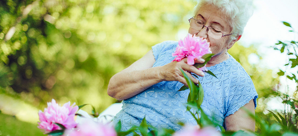 Eine ältere Frau riecht an Blume